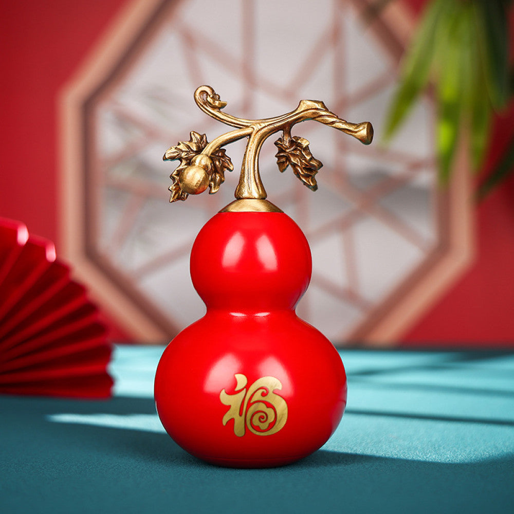 Traditional Chinese red gourd ornament with golden "Fu" character and vine details, placed on a teal surface with a red fan and lattice window in the background