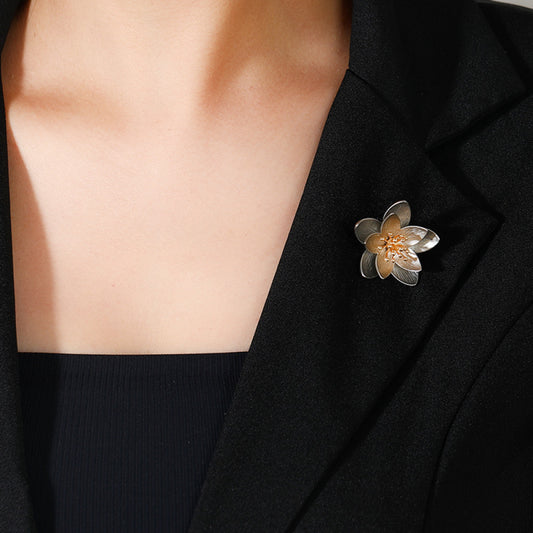 This elegant floral brooch features a striking two-tone metal design, with silver-toned outer petals and warm gold inner petals showcasing a delicate, brushed texture. The center is adorned with a cluster of sparkling clear crystals, adding a touch of luminous sophistication. Perfect for elevating blazers, scarves, or everyday outfits, this piece blends modern design with timeless floral charm.01
