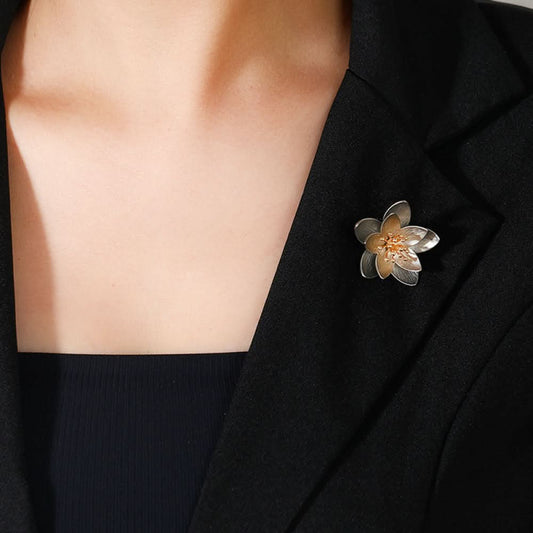 This elegant floral brooch features a striking two-tone metal design, with silver-toned outer petals and warm gold inner petals showcasing a delicate, brushed texture. The center is adorned with a cluster of sparkling clear crystals, adding a touch of luminous sophistication. Perfect for elevating blazers, scarves, or everyday outfits, this piece blends modern design with timeless floral charm.01