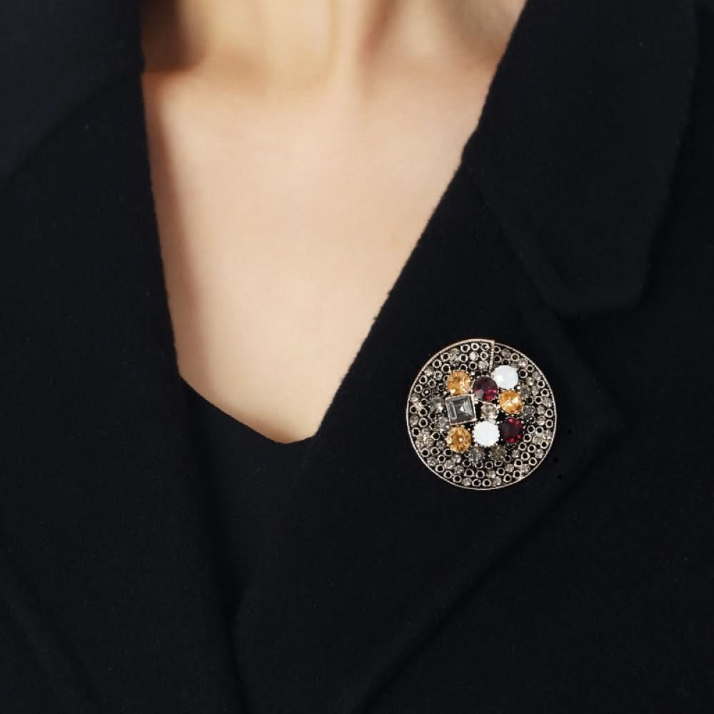 This collection of brooches exudes rich vintage charm, crafted on an antiqued bronze metal base and incorporating pearls, colored crystals, and clear gemstones. The circular brooch is intricately set with a dense array of small crystals and colored gemstones, opulent yet delicate. The arrow-shaped brooch carries a whimsical vintage tribal vibe, with a pearl drop pendant that adds depth. The large gemstone brooch is centered on a striking black stone, surrounded by pearls and colored gems for a commanding pr