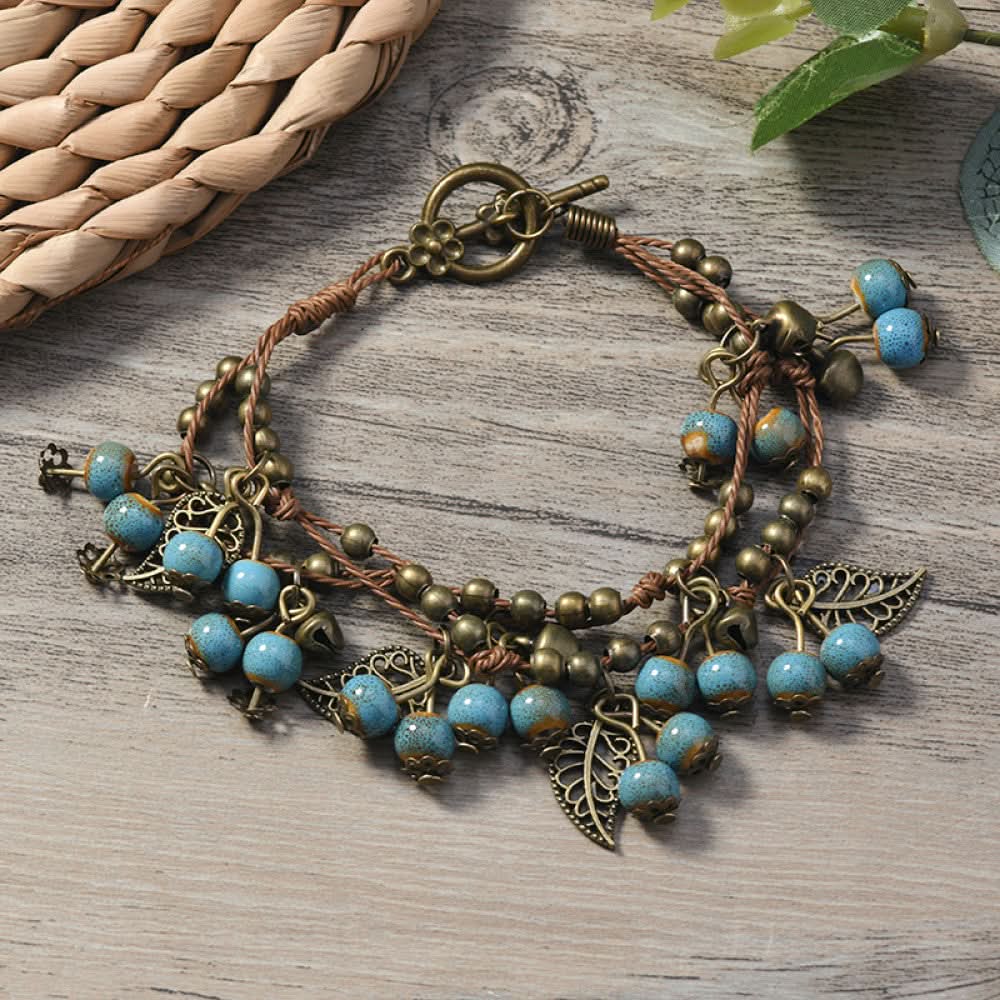 This vintage-style bracelet features a brown braided cord, adorned with antique bronze leaf charms and vibrant red berry-like beads, creating a nature-inspired, bohemian look. The toggle clasp ensures a secure fit, making it a striking accessory for any outfit 8