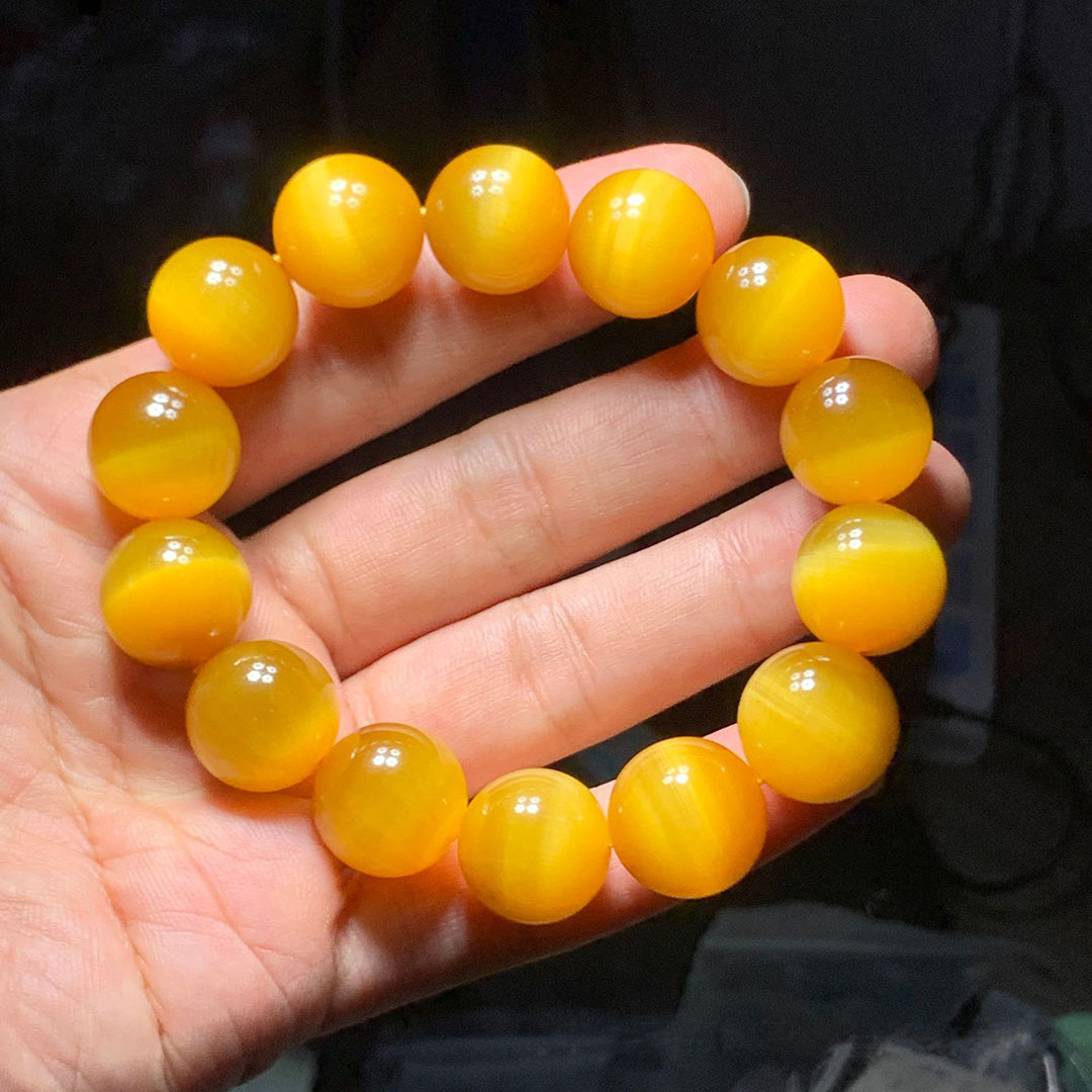 A hand - held yellow cat's eye gemstone bead bracelet, showcasing smooth, round beads with a distinct cat's eye effect and a vibrant yellow hue.