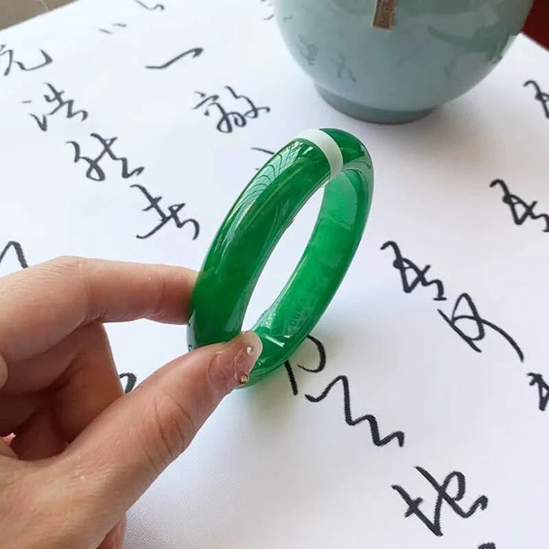 Emerald green jade bangle medium view held on calligraphy background, showing elegant round shape | DIY Jade