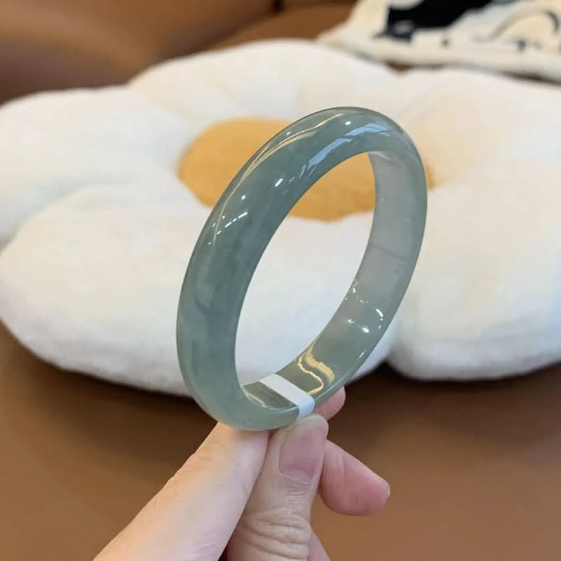Natural icy oil green jade bangle held by finger, showing smooth glossy finish against cozy decor | DIY Jade