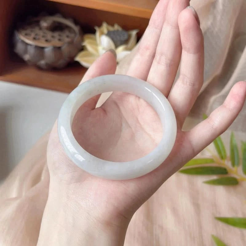 Natural icy white jade bangle held in hand with Chinese decor, showing smooth glossy finish | DIY Jade