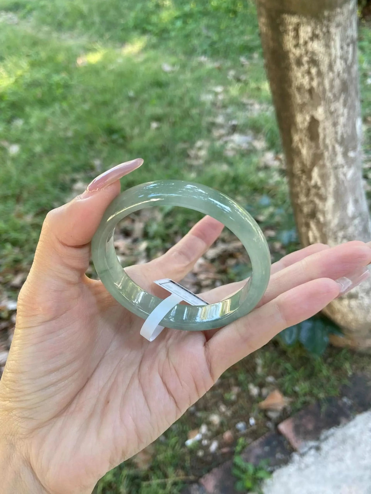 Light green jadeite bangle bracelet with tag, held in hand to show full ring shape | DIY Jade