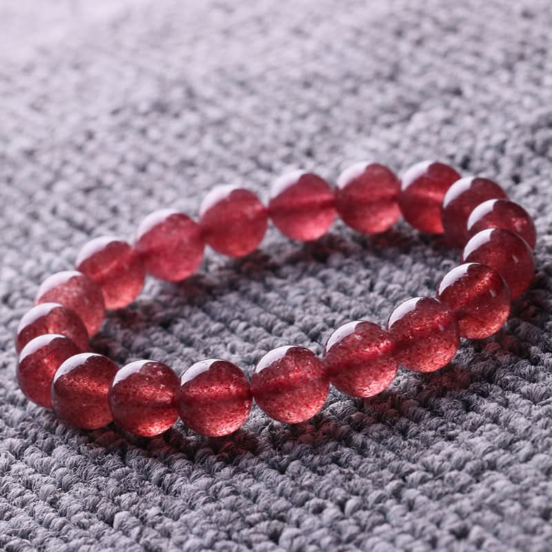 Natural pinkish-red strawberry quartz round bead bracelet with sparkling inclusions, displayed on textured fabric | DIY Jade