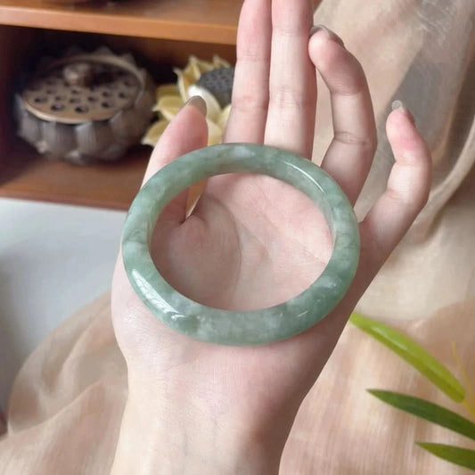 Pale green floating pattern jadeite bangle bracelet, full view held in hand with natural decor | DIY Jade