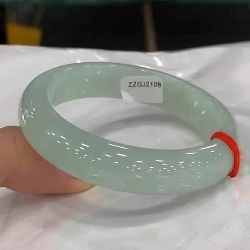 Pale green jade bangle with red string tag, showing glossy surface on white cloth | DIY Jade