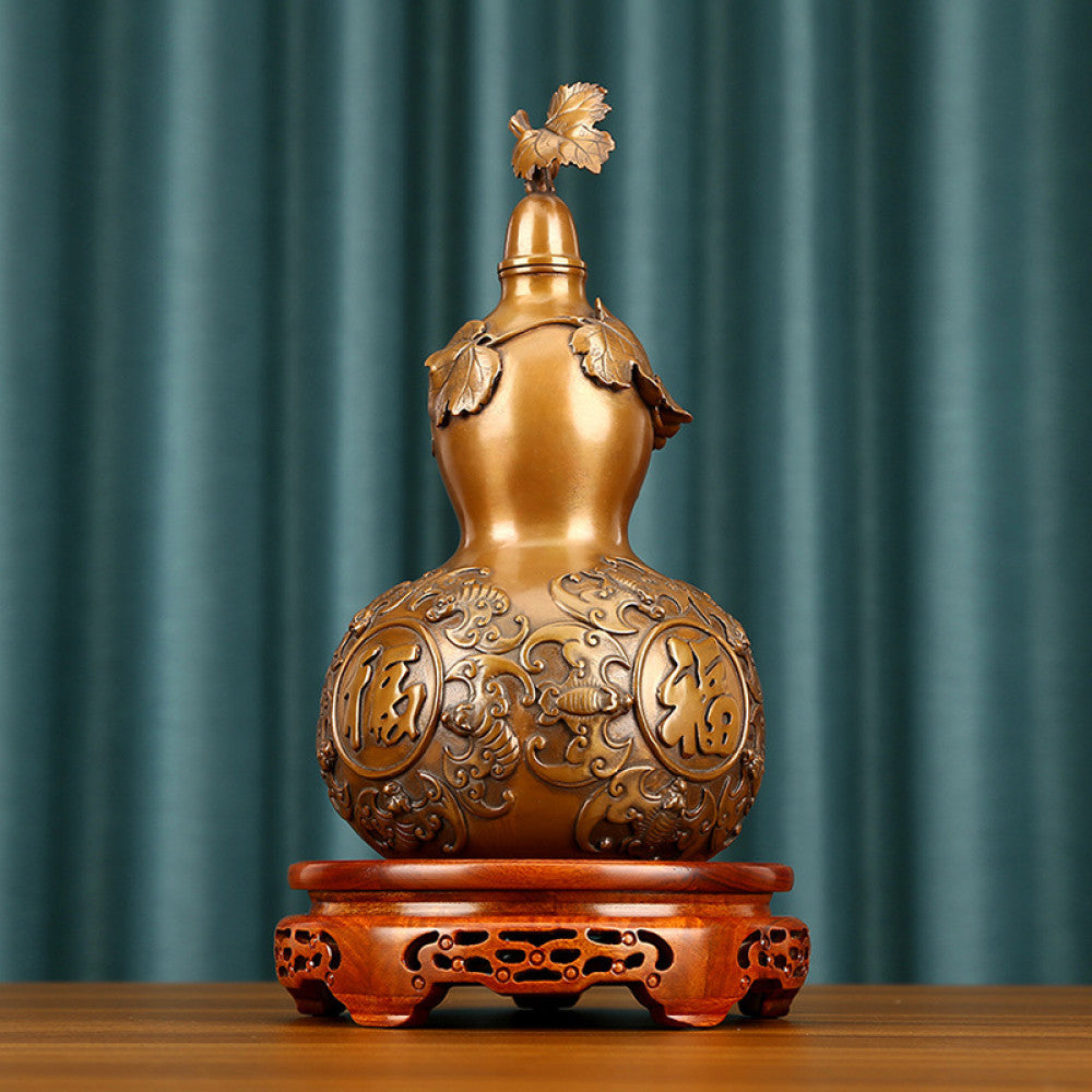 Traditional Chinese brass gourd decor with fortune characters and intricate carvings, placed on a wooden base against a teal curtain background