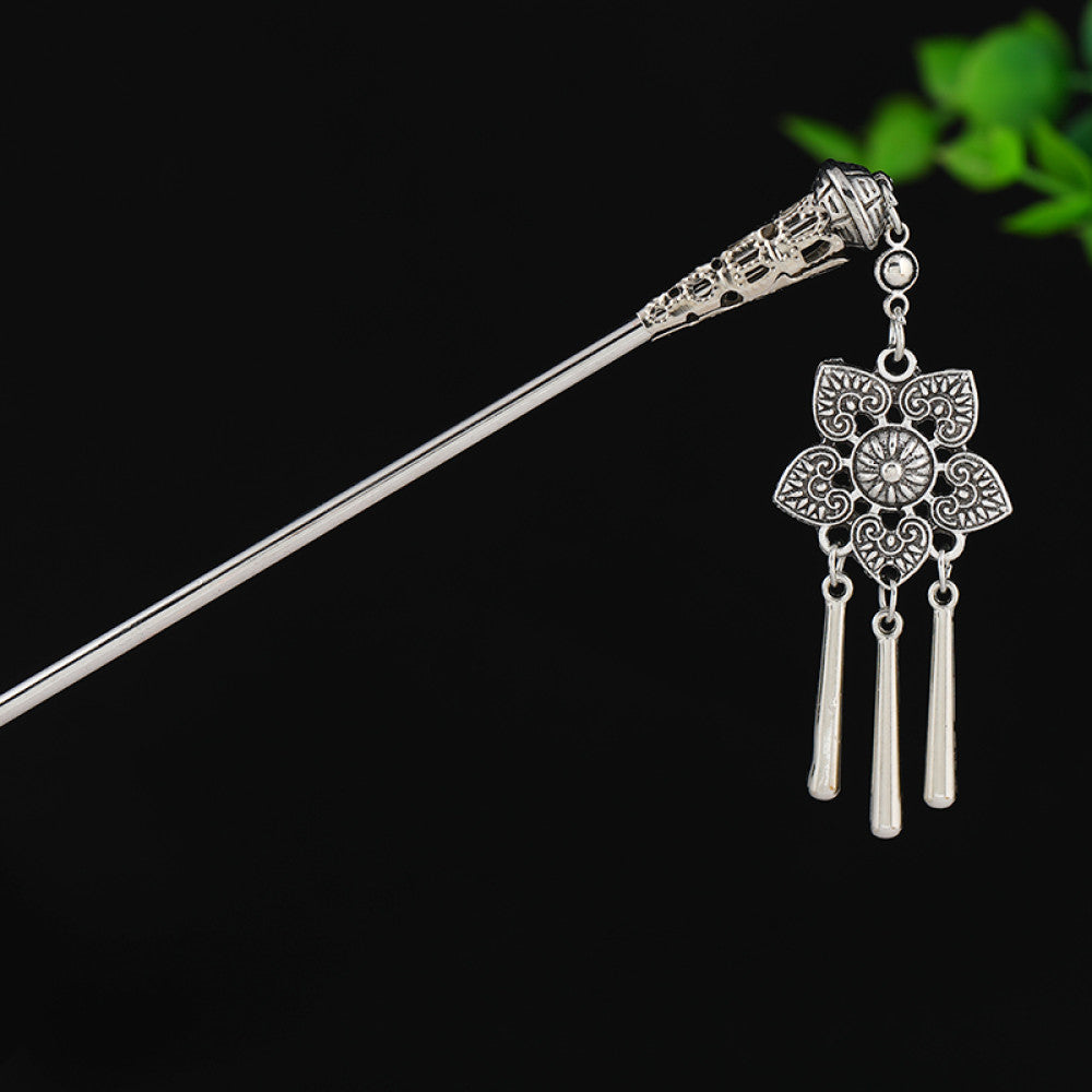 silver-tone hair stick featuring turquoise beads, an intricate round decorative element, and layered chain tassel fringe, displayed beside a white vessel green foliage 04