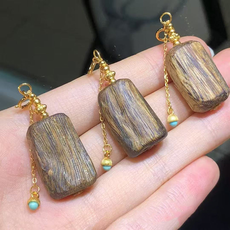 A pair of drop earrings featuring rectangular amberwood pendants, gold - plated chains, and small turquoise bead accents, held in a hand