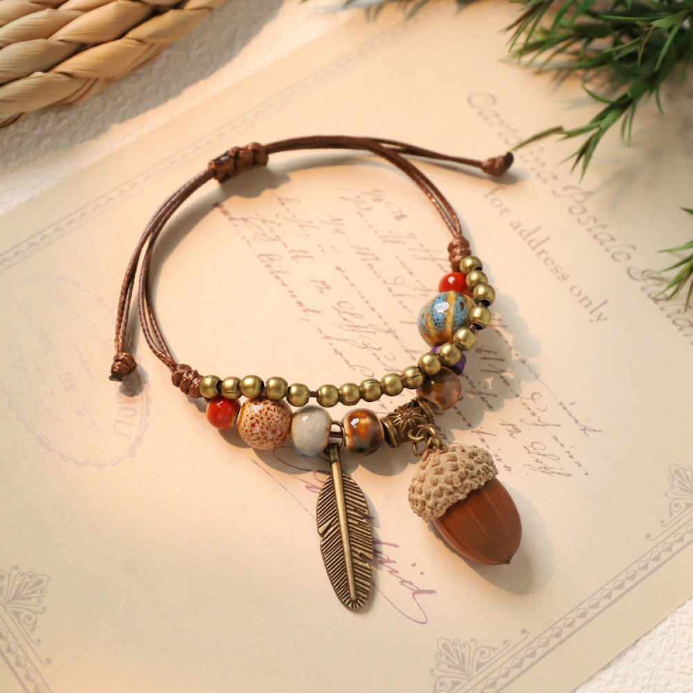 This bohemian bracelet features an adjustable brown cord, adorned with colorful beads, brass accents, and charming acorn & feather charms, bringing a whimsical, nature-inspired touch to your look