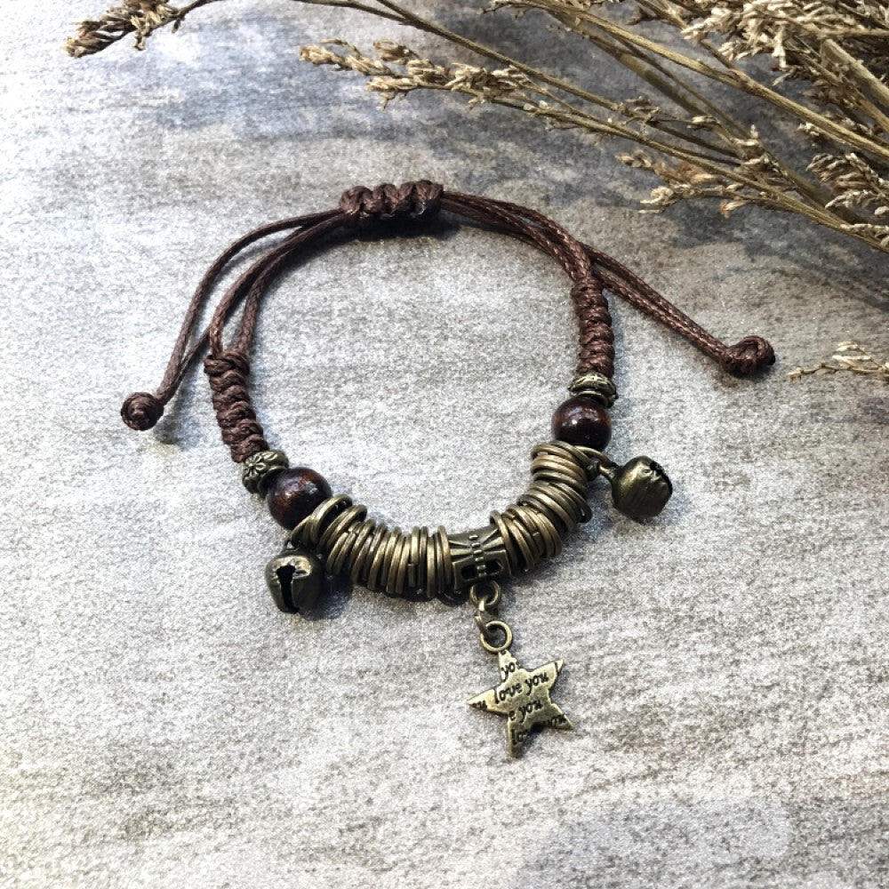This handmade bohemian bracelet features a brown braided cord, vintage bronze bells, a star charm, and adjustable knots for a perfect fit. A unique retro accessory for daily wear.