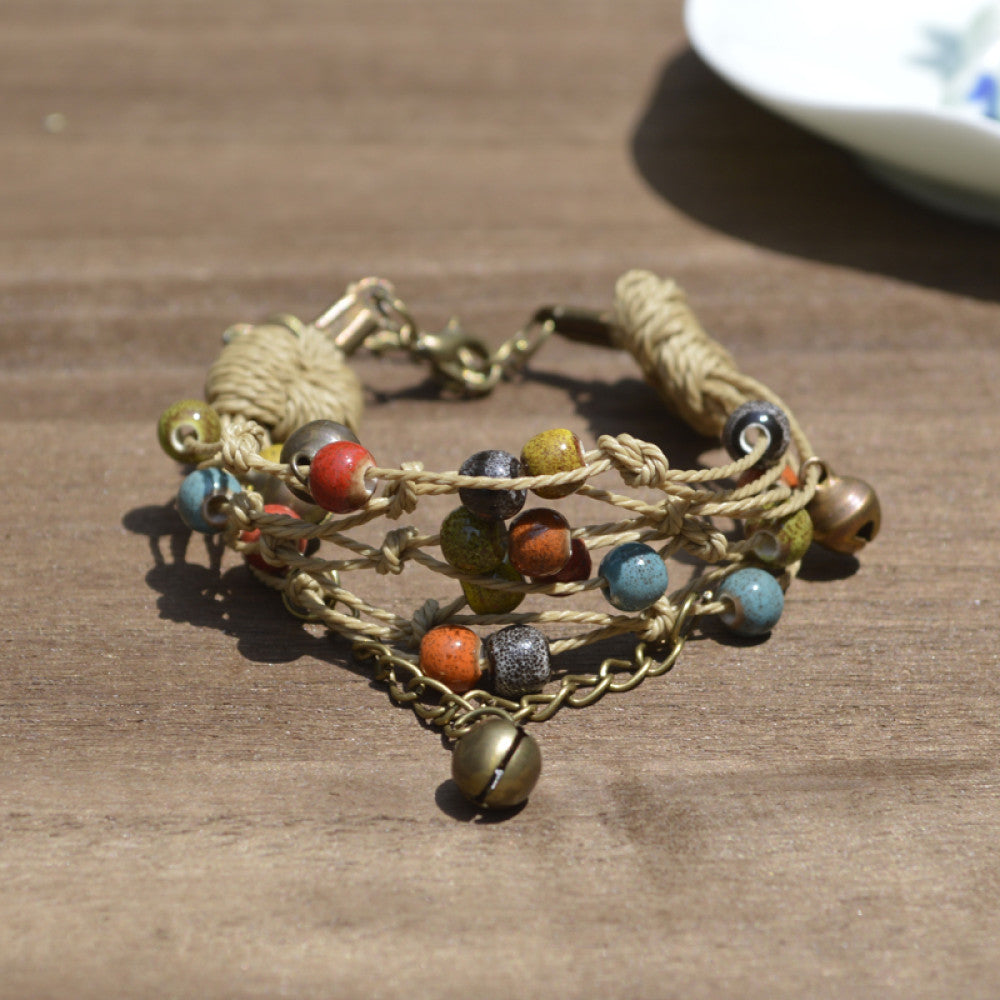 This bohemian multi-layer bracelet features vibrant ceramic beads woven on natural rope, accented with bronze bells and a chain layer. The adjustable clasp ensures a comfortable fit