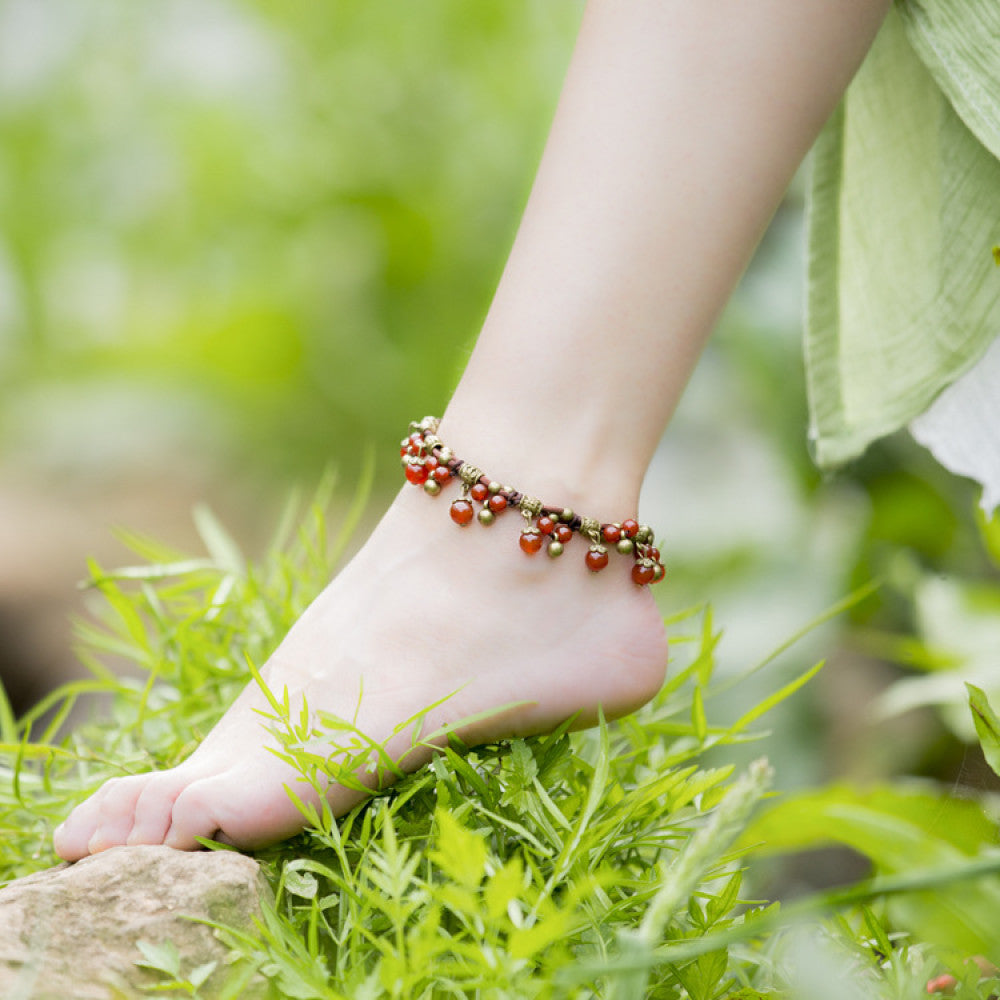 This bohemian anklet features vibrant red beads and delicate green accents on a brown cord, designed for a lightweight, nature-inspired summer look. The adjustable design ensures a comfortable fit for casual, outdoor wear