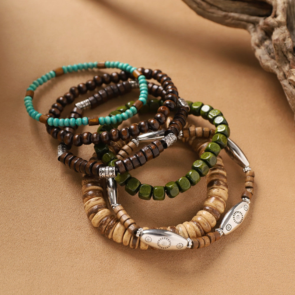 This bohemian stackable bracelet set features multiple layered strands in earthy tones, including turquoise, dark brown, green, and light brown beads, accented with decorative silver elements. The mix of natural materials and ethnic-inspired details creates a rich, textured look, perfect for layering to elevate casual outfits