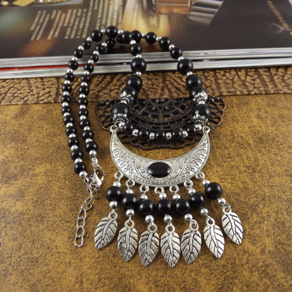 Vintage black beaded necklace with intricate silver-toned leaf tassel and crescent pendant, featuring black beads and gothic tribal design, ideal for bohemian goth fashion, showcased on a textured surface with vintage accents