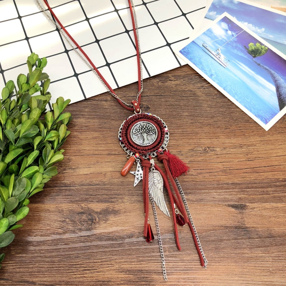 Vintage bohemian blue dreamcatcher necklace with tassel, feather, and geometric accents, displayed on a wooden surface with grid paper and greenery, ideal for boho fashion enthusiasts 01