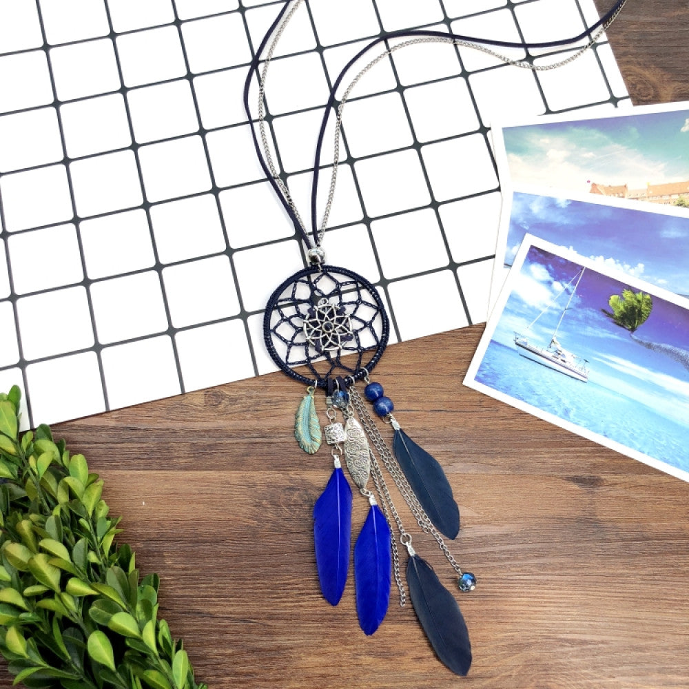 Vintage bohemian blue dreamcatcher necklace with tassel, feather, and geometric accents, displayed on a wooden surface with grid paper and greenery, ideal for boho fashion enthusiasts 06
