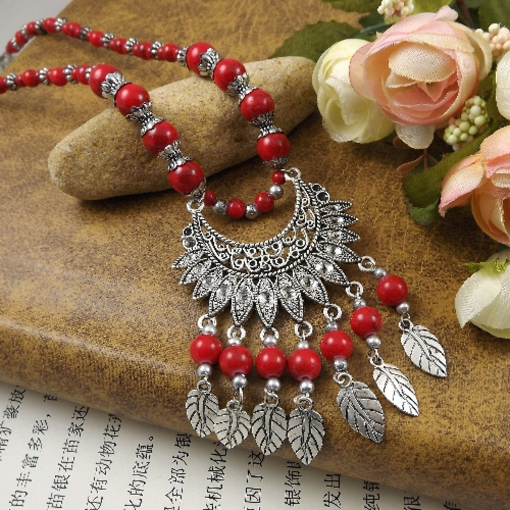 Vibrant colorful beaded necklace with intricate silver-toned leaf tassel and crescent pendant, featuring a mix of bright beads, ideal for bohemian fashion, showcased on a textured surface with floral accents 03