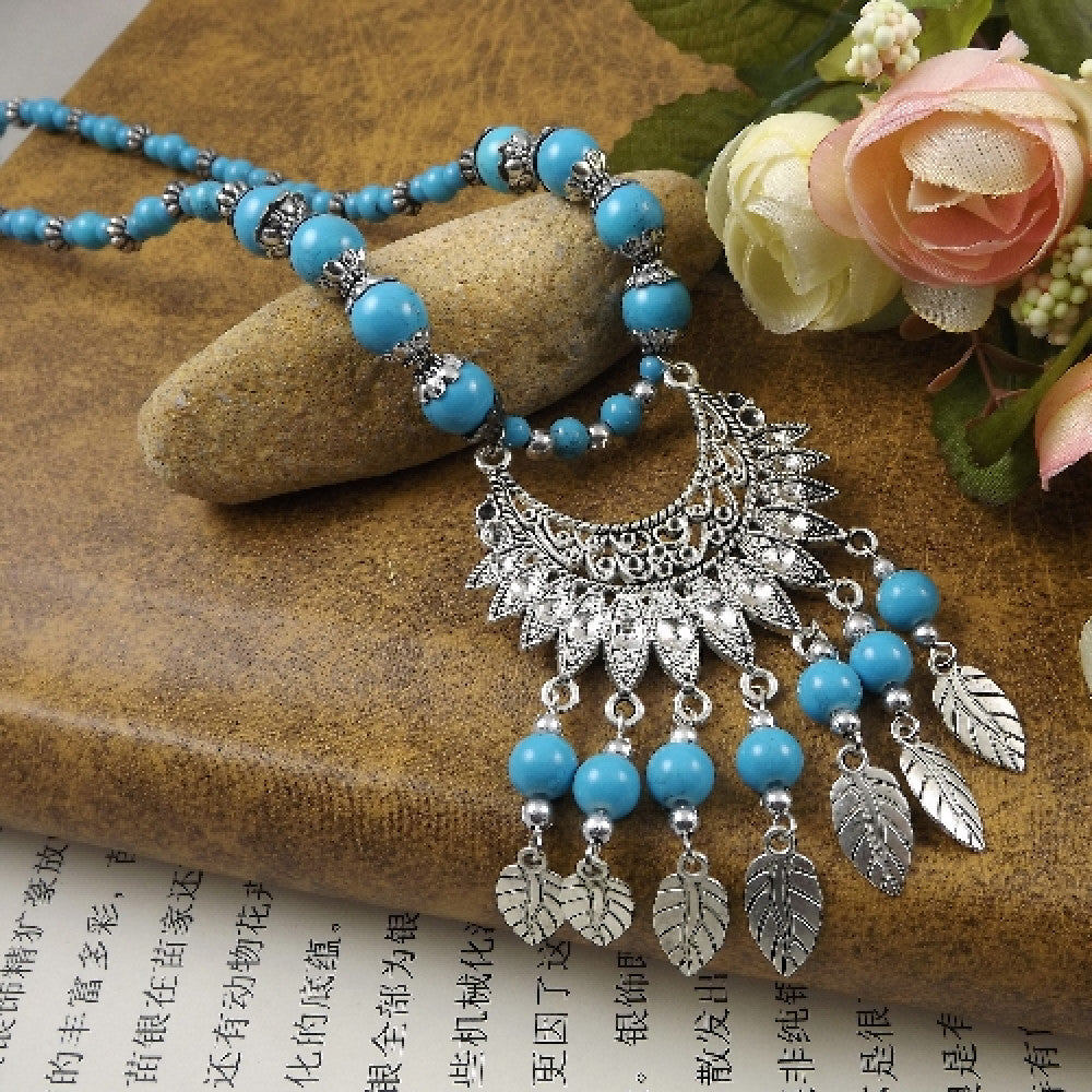 Vibrant colorful beaded necklace with intricate silver-toned leaf tassel and crescent pendant, featuring a mix of bright beads, ideal for bohemian fashion, showcased on a textured surface with floral accents 06