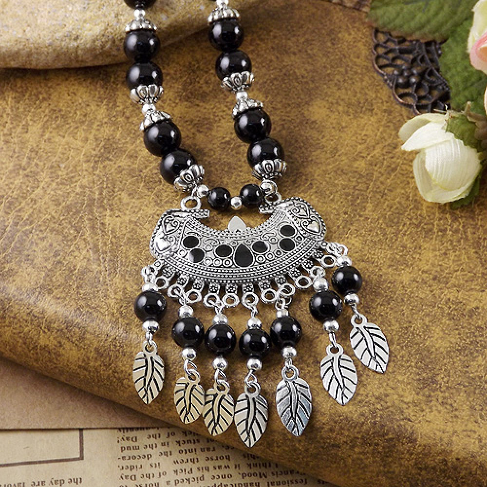 Vibrant colorful beaded necklace with intricate silver-toned leaf tassel pendant, featuring a mix of bright beads and vintage tribal design, ideal for bohemian fashion, showcased on a textured surface with floral accents 03