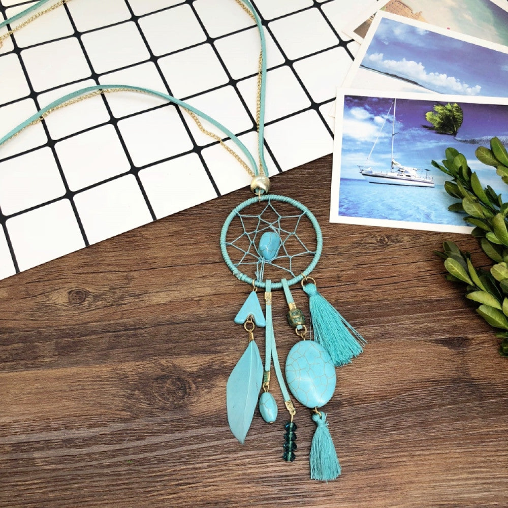 Vintage bohemian dreamcatcher necklace with feather, stone, and tassel accents, displayed on a wooden surface with grid paper and greenery, ideal for spiritual boho fashion enthusiasts 01