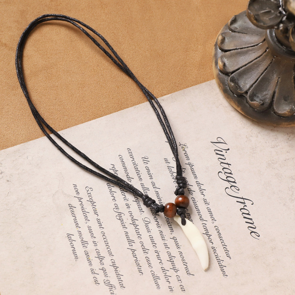 Vintage bohemian ethnic necklace with animal tooth pendant, black cord, and wood bead accents, displayed on vintage paper with decorative elements, ideal for tribal and boho fashion enthusiasts
