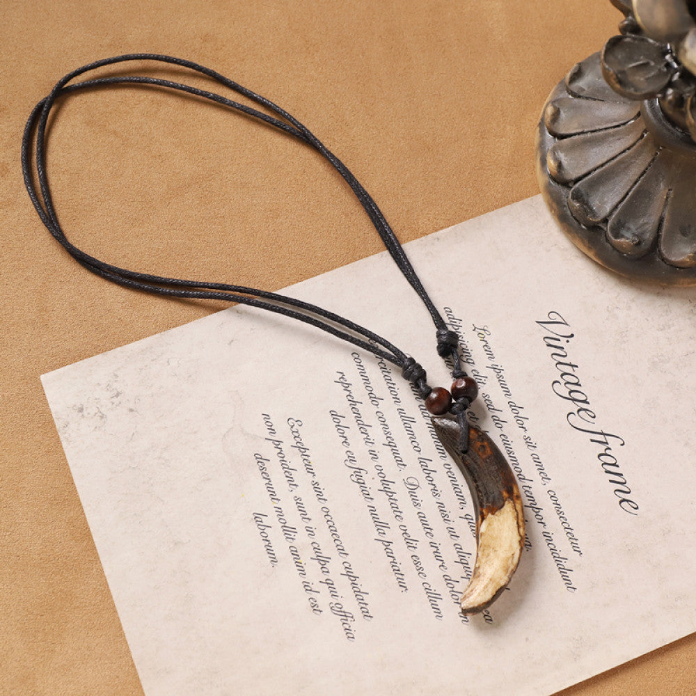 Vintage bohemian ethnic necklace with animal tooth pendant, black cord, and wood bead accents, displayed on vintage paper with decorative elements, ideal for tribal and boho fashion enthusiasts 01