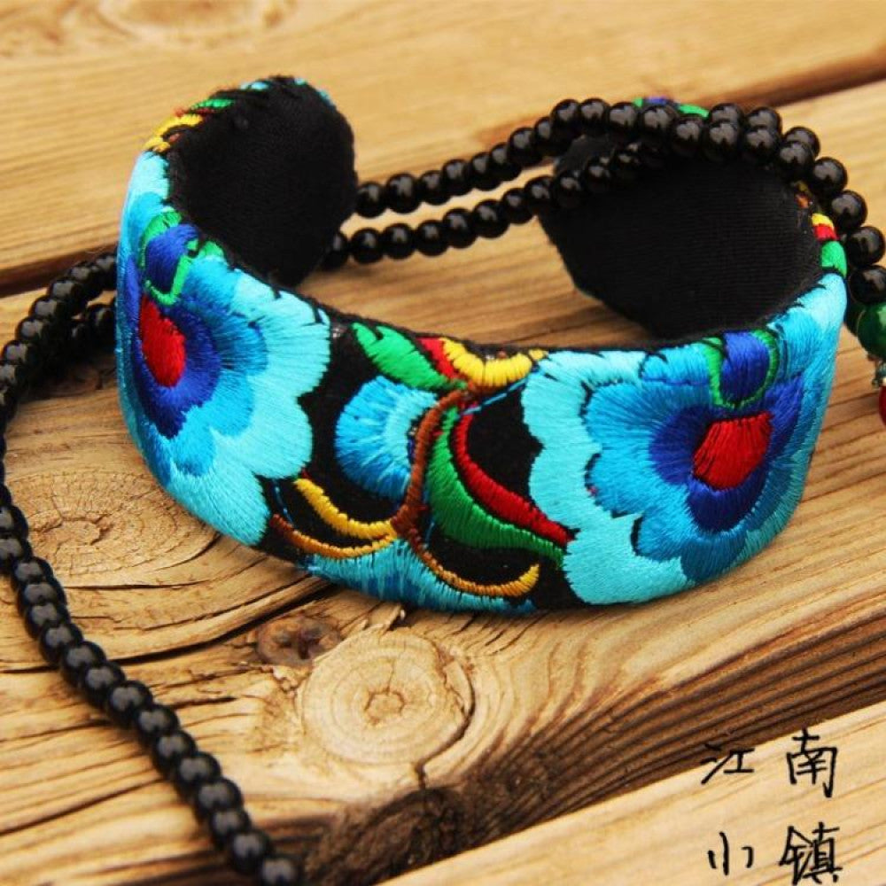 Vintage bohemian ethnic embroidered cuff bracelet with colorful floral design and black bead chain, displayed on wooden surface, ideal for boho and ethnic fashion enthusiasts