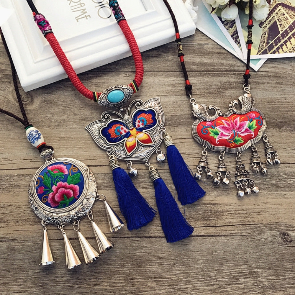 Assorted bohemian vintage ethnic embroidered necklace set with floral, butterfly designs, tassels, and silver accents, displayed on a wooden surface with decorative elements, ideal for boho fashion enthusiasts