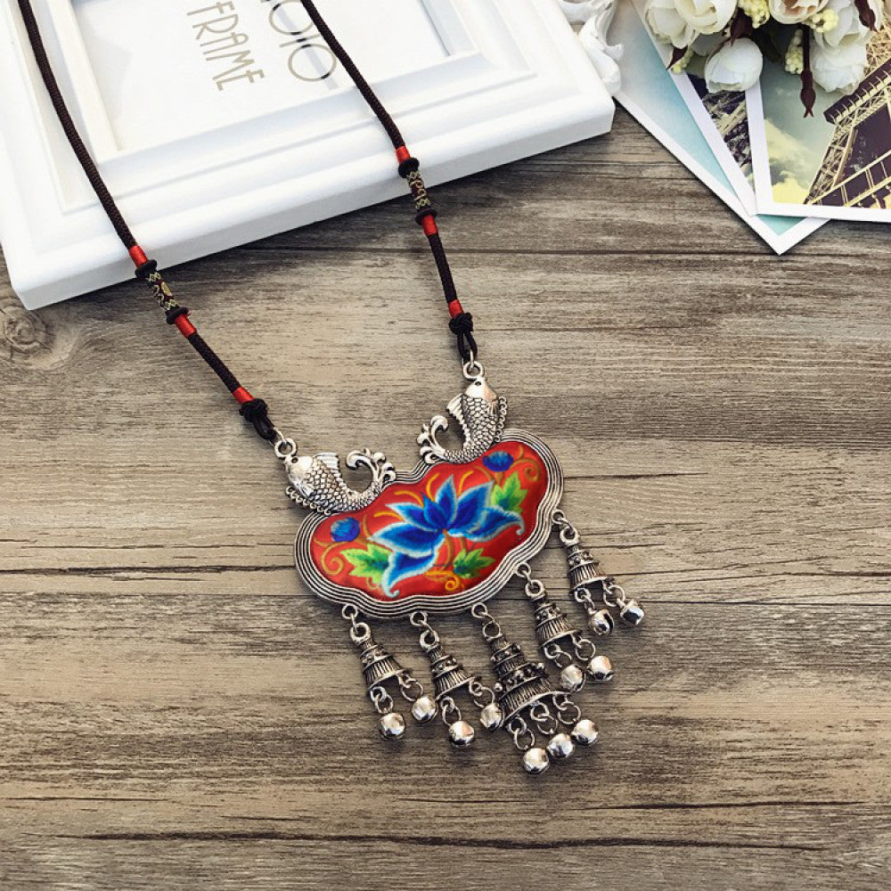 Vintage bohemian ethnic necklace with colorful enamel floral pendant and silver bell tassels, displayed on a wooden surface with decorative accents, ideal for boho fashion enthusiasts