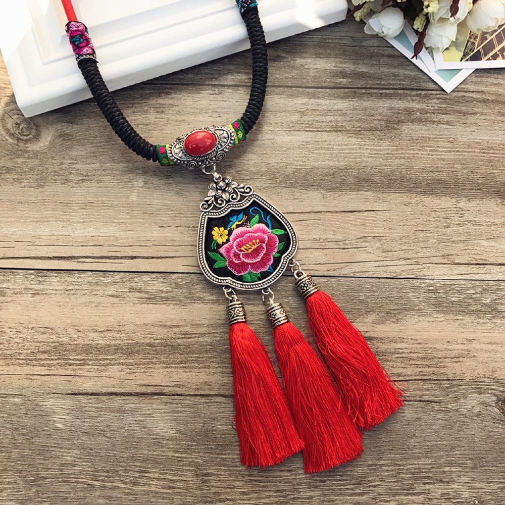 Vintage bohemian ethnic necklace with colorful enamel floral pendant and silver bell tassels, displayed on a wooden surface with decorative accents, ideal for boho fashion enthusiasts 01