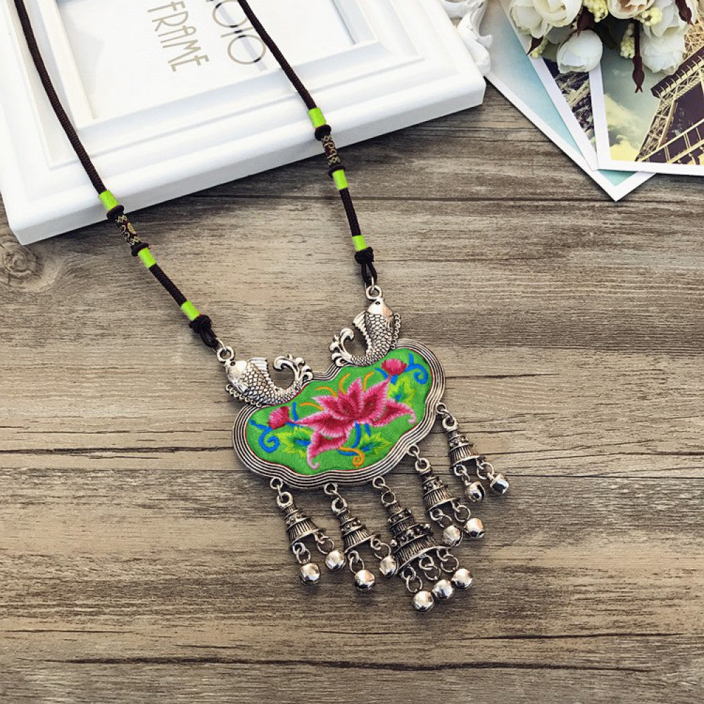 Vintage bohemian ethnic necklace with colorful enamel floral pendant and silver bell tassels, displayed on a wooden surface with decorative accents, ideal for boho fashion enthusiasts 06