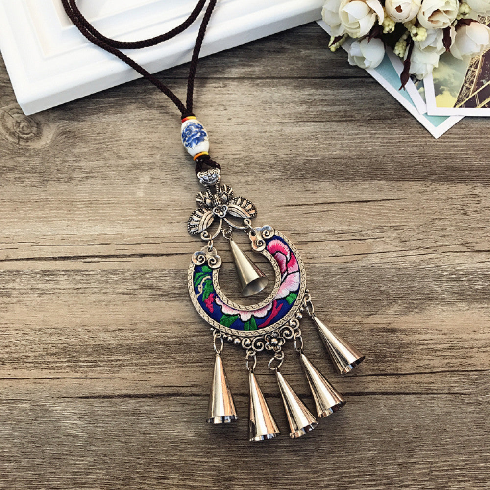Vintage bohemian ethnic necklace with colorful enamel floral pendant and silver bell tassels, displayed on a wooden surface with decorative accents, ideal for boho fashion enthusiasts 08