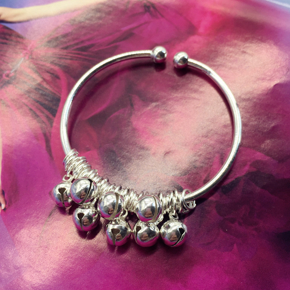 Vintage bohemian ethnic silver-tone bangle adorned with heart-shaped bell charms, displayed on a pink floral background, ideal for boho fashion enthusiasts