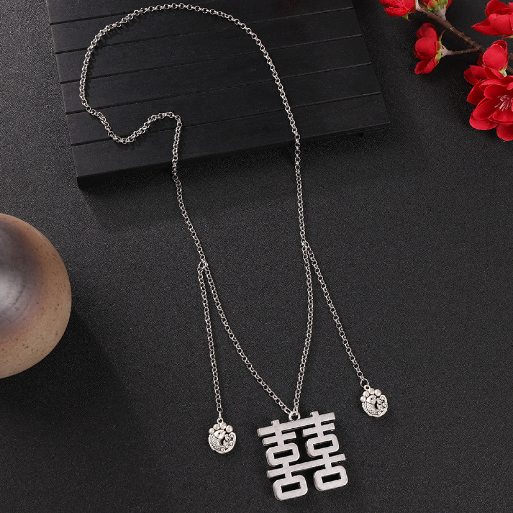 Vintage bohemian ethnic silver-tone necklace with Double Happiness pendant and filigree details, displayed on a dark background with red flowers, ideal for boho fashion and cultural-inspired styling