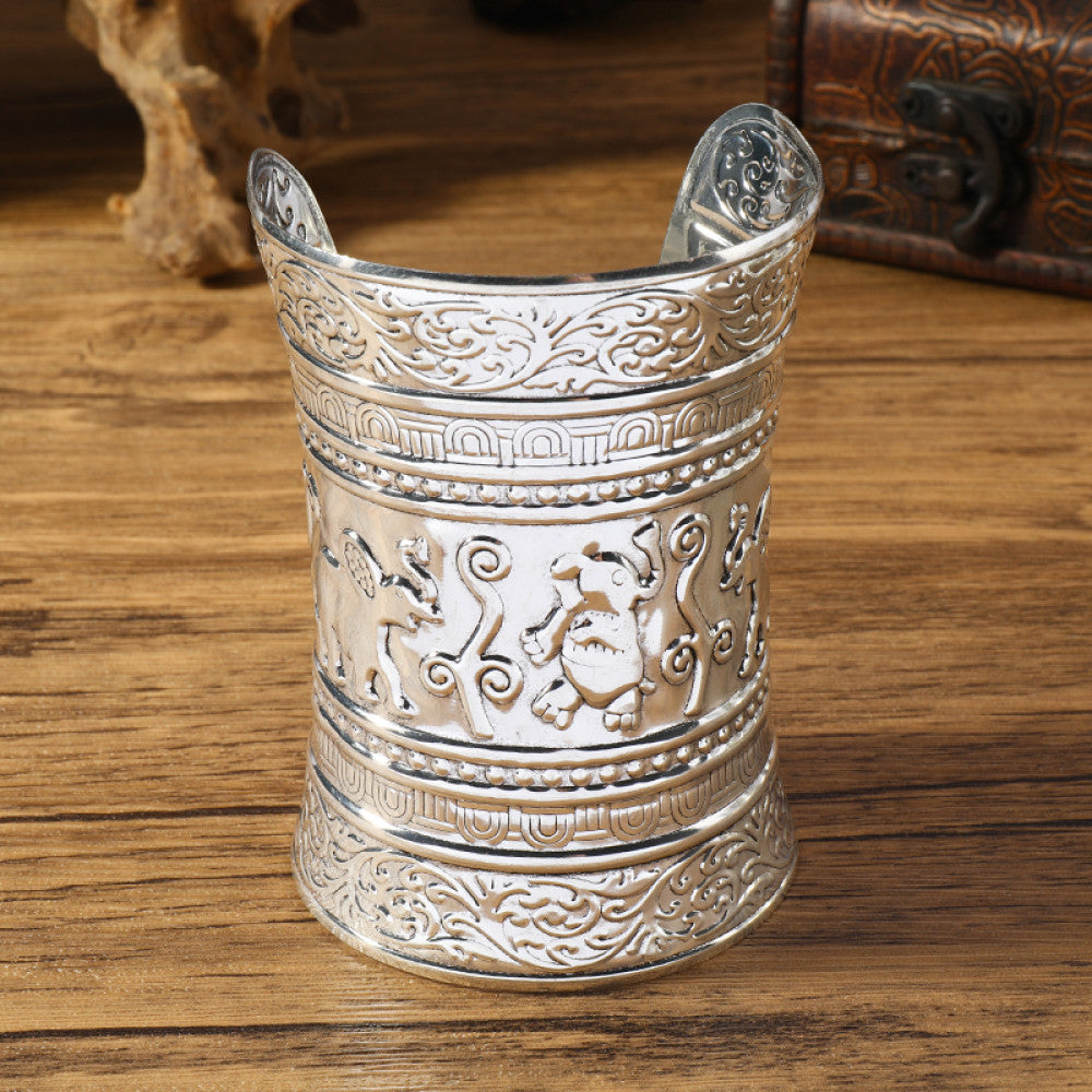 Vintage bohemian ethnic silver-tone cuff bracelet with intricate tribal animal engravings, displayed on a wooden surface with decorative elements, ideal for boho and ethnic fashion enthusiasts