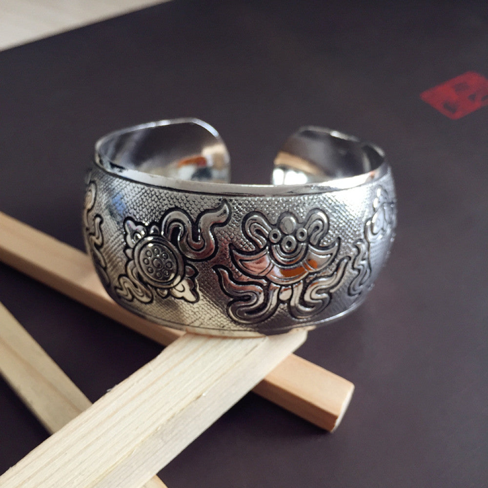 Vintage bohemian ethnic silver-tone cuff bracelet with intricate traditional motif engravings, displayed on wooden accents, ideal for boho and ethnic fashion enthusiasts