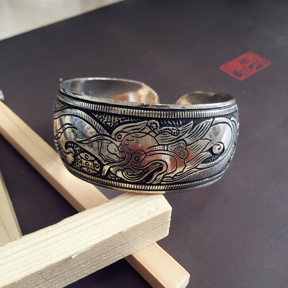 Vintage bohemian ethnic silver-tone cuff bracelet with intricate traditional motif engravings, displayed on wooden accents, ideal for boho and ethnic fashion enthusiasts 02