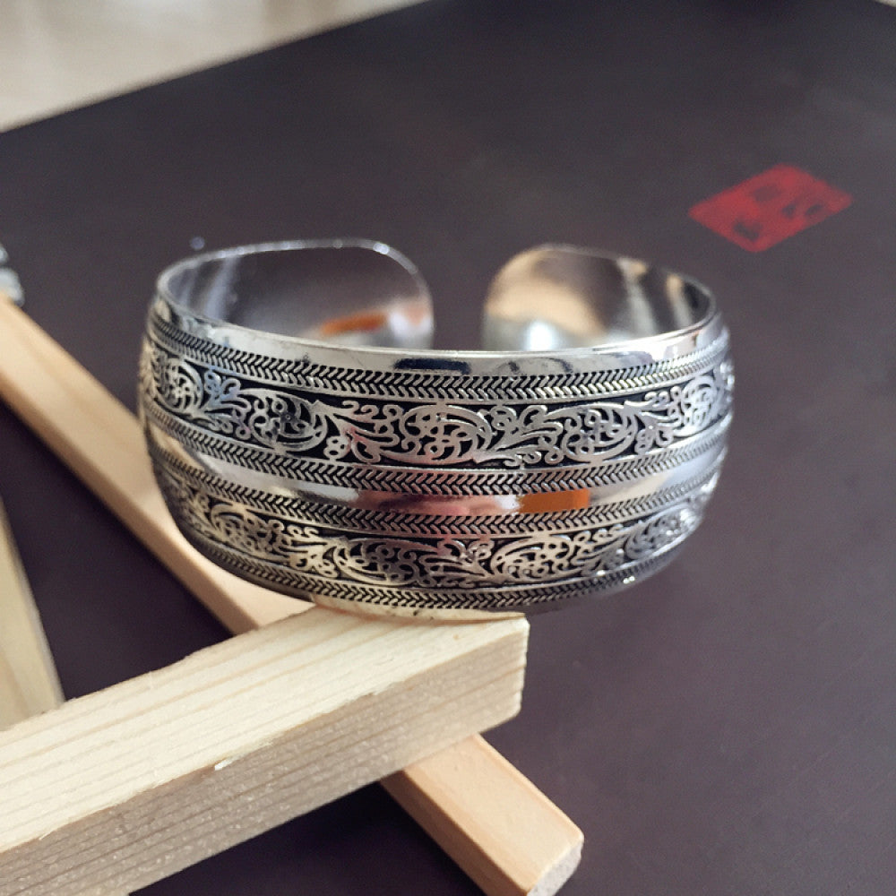 Vintage bohemian ethnic silver-tone cuff bracelet with intricate traditional motif engravings, displayed on wooden accents, ideal for boho and ethnic fashion enthusiasts 13