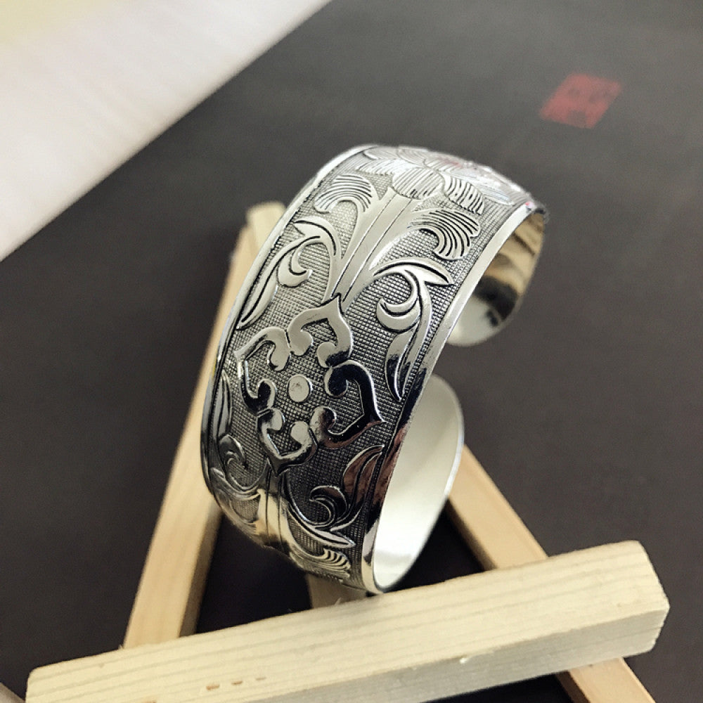 Vintage bohemian ethnic silver-tone engraved filigree cuff bracelet with intricate floral designs, displayed on wooden accents, ideal for boho and ethnic fashion enthusiasts