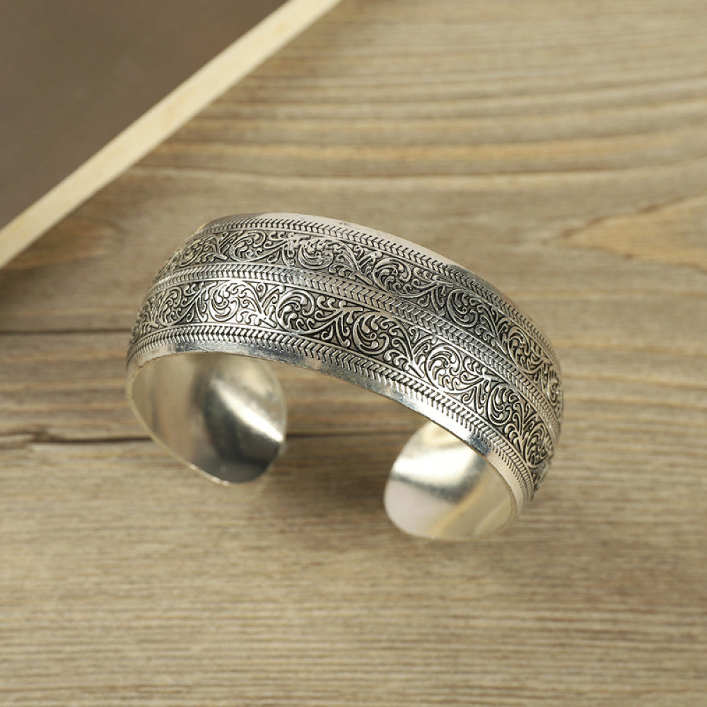 Vintage bohemian ethnic silver-tone engraved filigree cuff bracelet with intricate floral designs, displayed on wooden accents, ideal for boho and ethnic fashion enthusiasts 11
