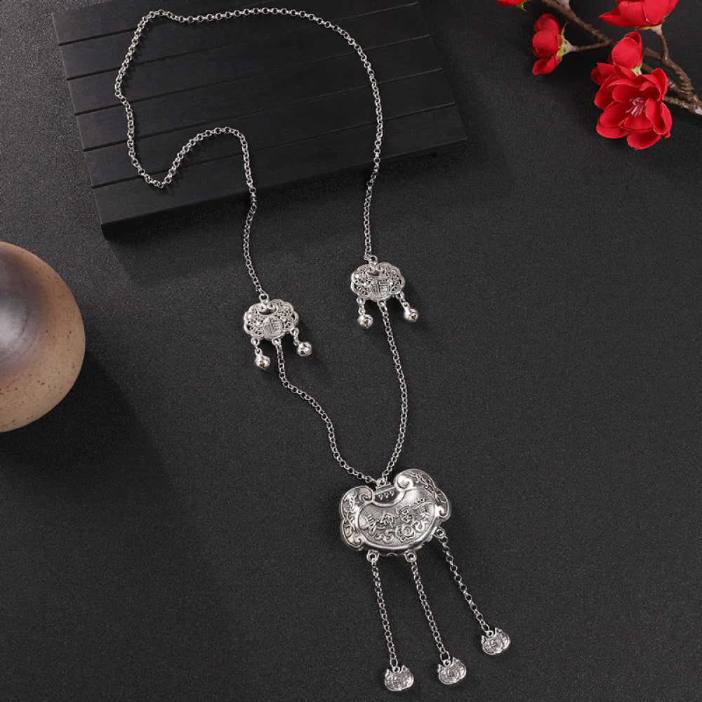 Vintage bohemian ethnic silver-tone necklace with intricate filigree, tassel bells, and ornate pendant, displayed on a dark background with red flowers and decorative accents, ideal for boho and ethnic fashion enthusiasts