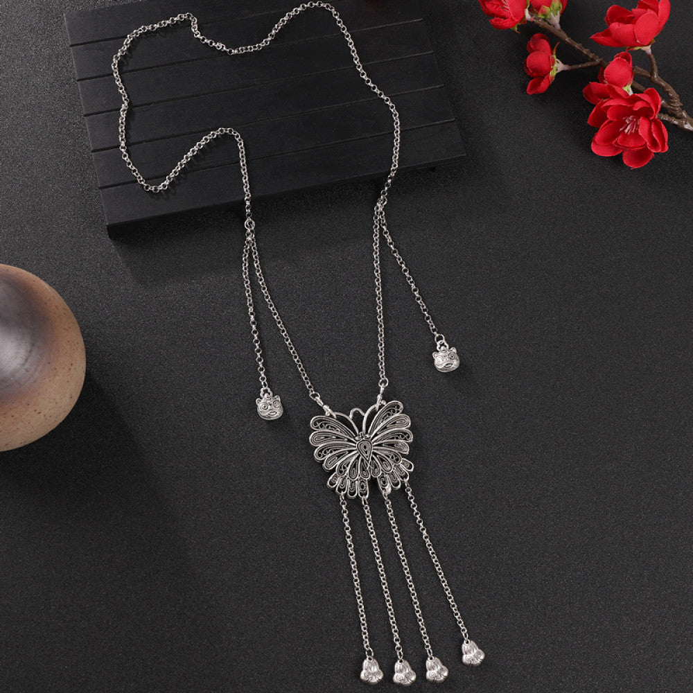 Vintage bohemian ethnic silver-tone necklace with intricate filigree, tassel bells, and ornate pendant, displayed on a dark background with red flowers and decorative accents, ideal for boho and ethnic fashion enthusiasts 01