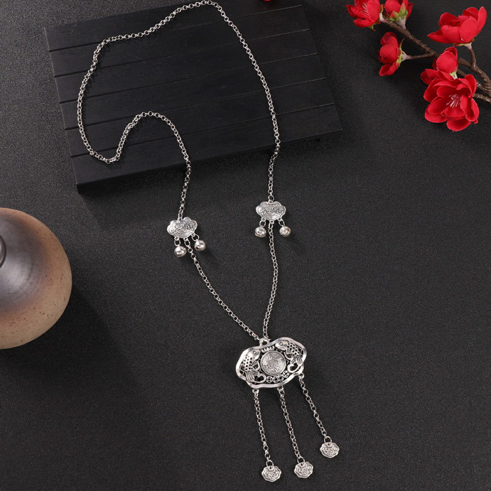 Vintage bohemian ethnic silver-tone necklace with intricate filigree, tassel bells, and ornate pendant, displayed on a dark background with red flowers and decorative accents, ideal for boho and ethnic fashion enthusiasts 03