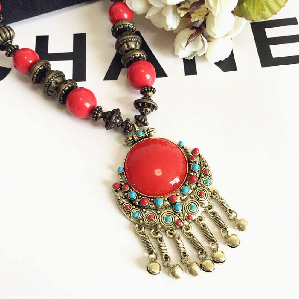 Vintage bohemian ethnic necklace with large red pendant, turquoise details, and tassel design, featuring antique bronze finish, ideal for boho fashion, displayed with floral and text accents against a white background