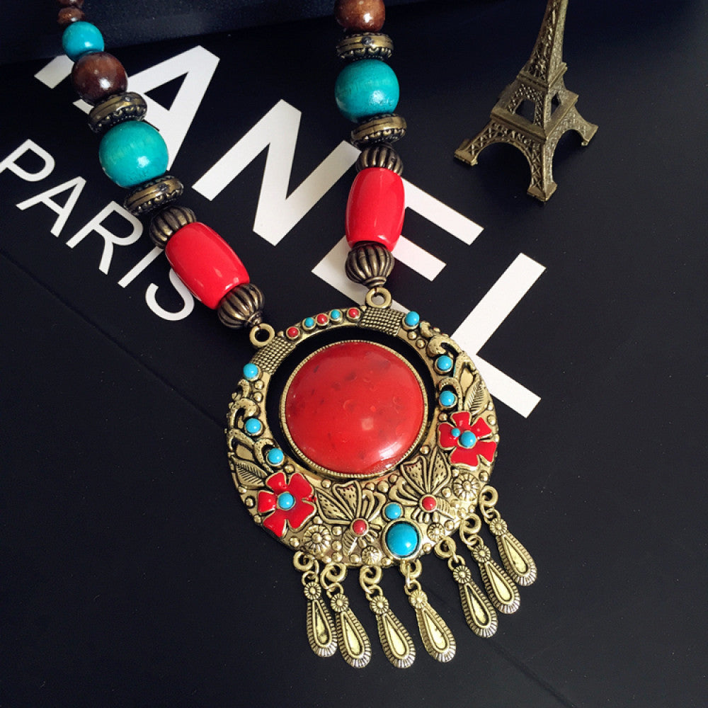 Vintage bohemian ethnic necklace with red pendant, turquoise accents, and tassel design, featuring antique bronze details, displayed against a black background with fashion text and Eiffel Tower accent, ideal for boho fashion enthusiasts