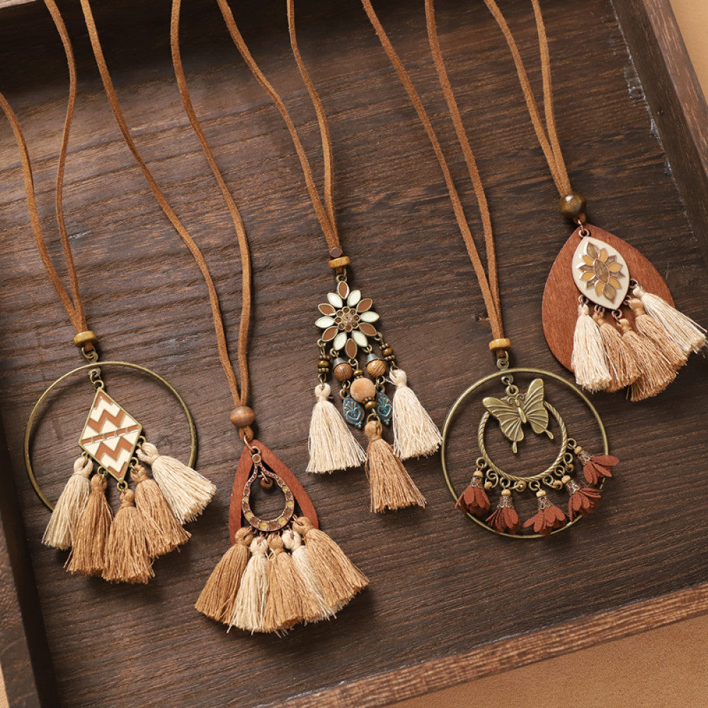 Assorted bohemian vintage tassel necklace set with geometric, butterfly, and floral pendants, featuring earthy tones and fringe details, displayed in a wooden tray, ideal for boho fashion enthusiasts